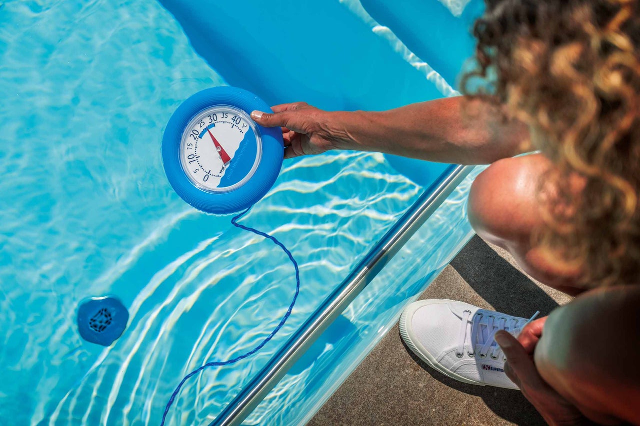 Een persoon meet de temperatuur in een zwembad met een zwembadthermometer.