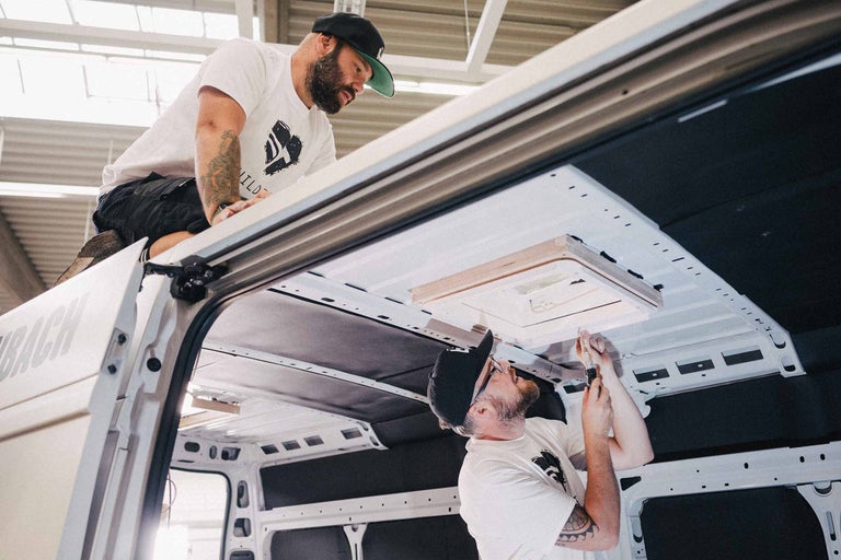Twee mannen monteren een dakraam in een bestelwagen.