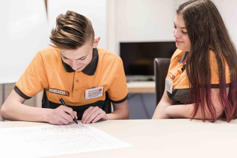 Twee Hornbach medewerkers zitten aan een tafel. Een van de twee schrijft iets op een vel papier.