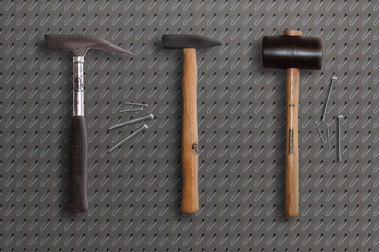 Drie hamers en enkele spijkers liggen op een geperforeerd metalen oppervlak.