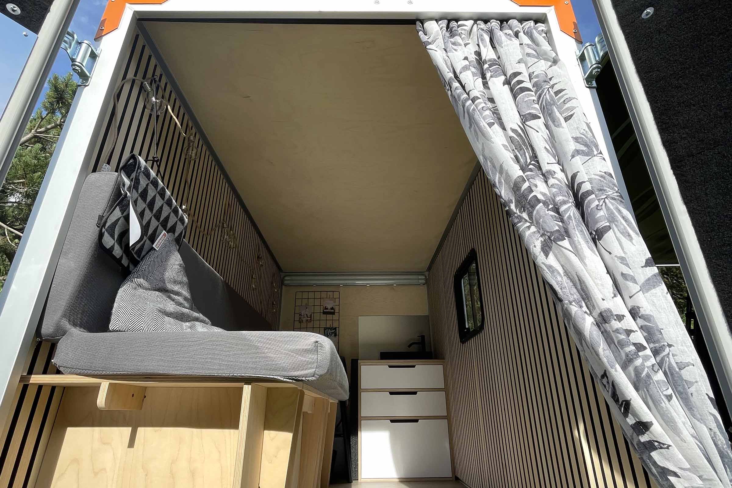 Interieur van een bestelwagen met bed, gordijnen en opbergruimte