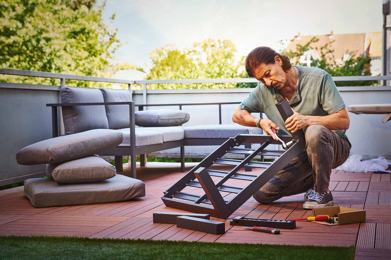 Vrouw schuurt houten plank buiten met schuurblok op een werkbank