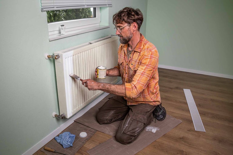 Man schildert radiator met kwast en verf.