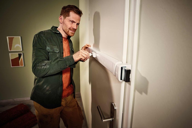 Een man installeert een witte deurintercom op een deur