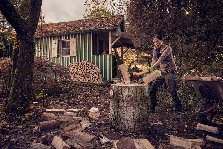 Een vrouw hakt hout met een bijl voor een houthok in een tuin.