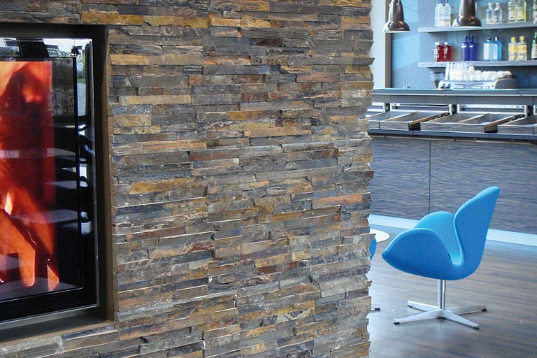 Wanddecoratie met natuursteenstrips naast open haard en blauwe zitmogelijkheid.