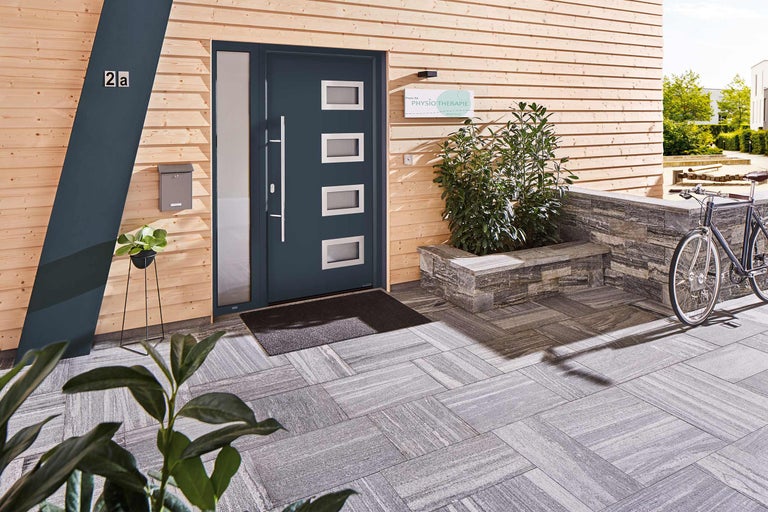 Buitenaanzicht van een huis met houten wand, voordeur met ramen, brievenbus en stenen bestrating