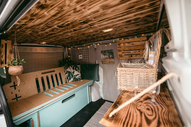 Interieur van een omgebouwde bestelwagen met houten plafond, bank en picknickmand