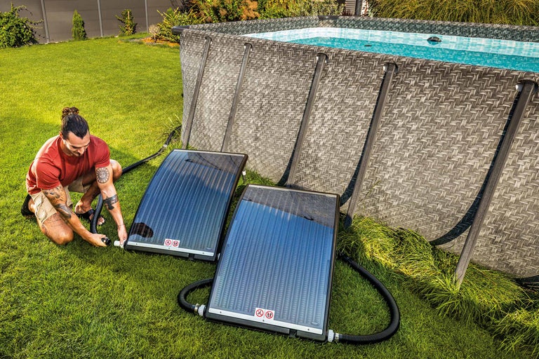 Een man installeert zonnecollectoren naast een zwembad in de tuin voor zwembadverwarming.