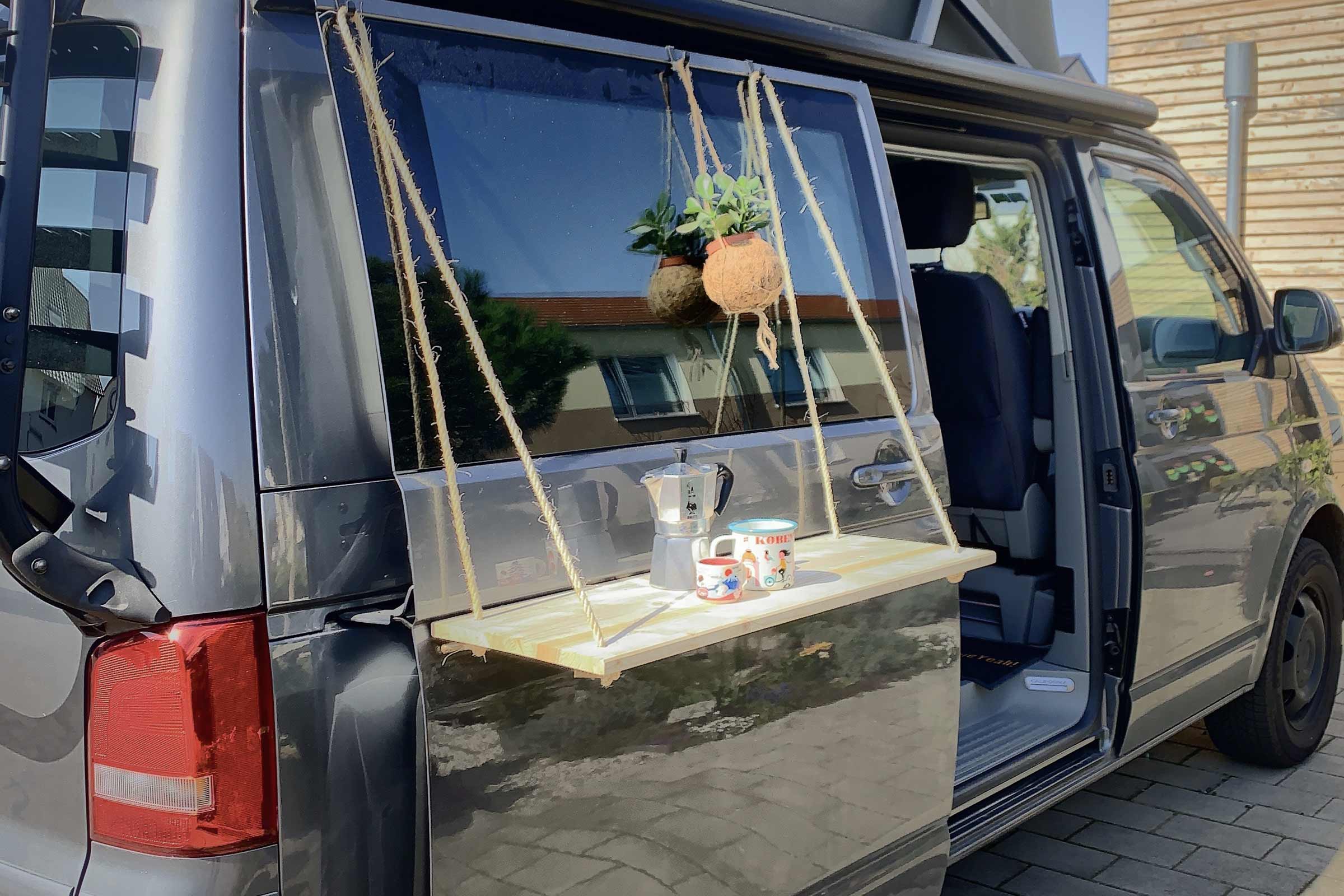 Kampeerauto met aan de achterklep bevestigde hangtafel met drankjes en plant