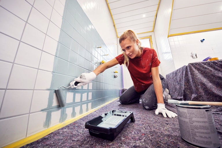 Een persoon schildert tegels met een verfroller.