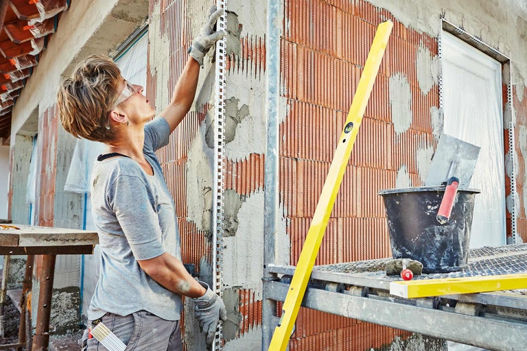 Vrouw monteert pleisterprofielen op een muur van bakstenen met mortel