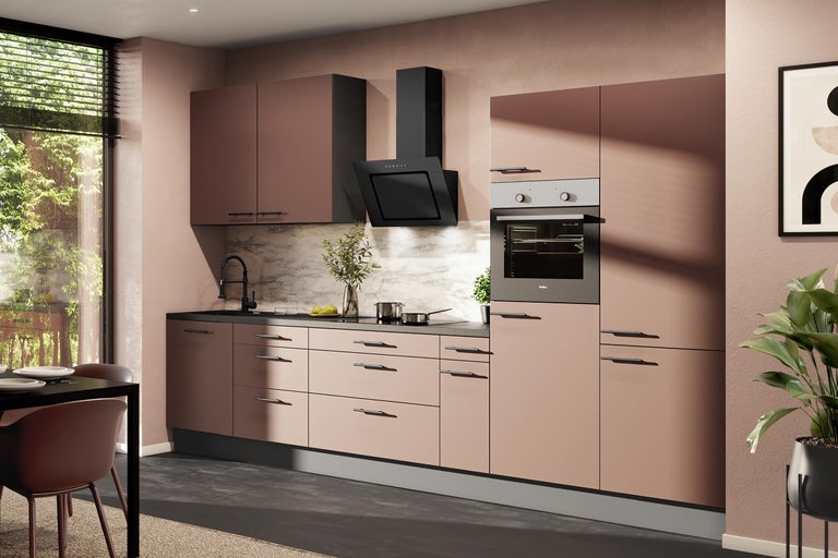 Moderne inbouwkeuken in oudroze met zwarte handgrepen, apparatuur, afzuigkap, oven en marmeren achterwand.