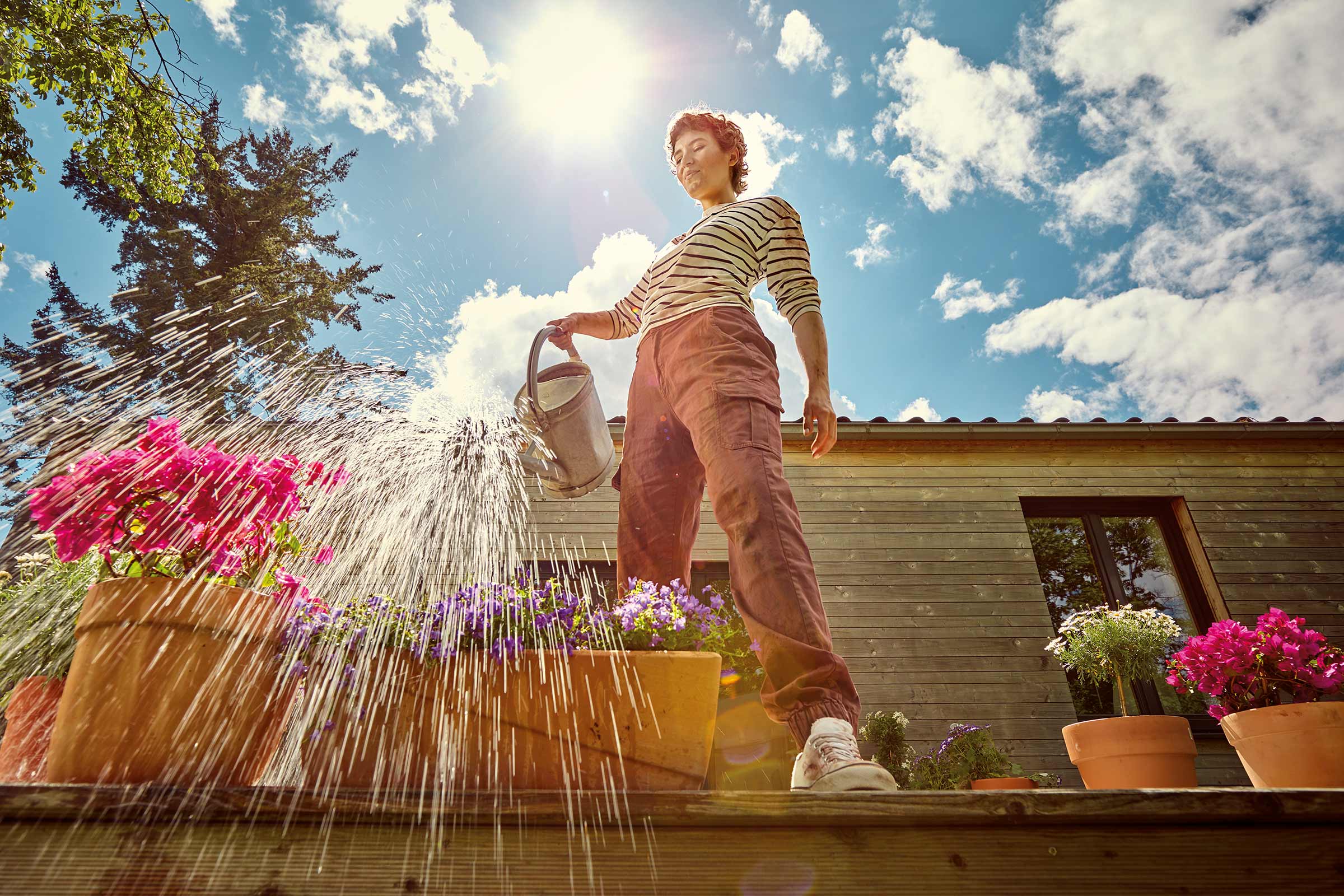 Vrouw geeft bloemen water met een gieter op een terras voor een huis