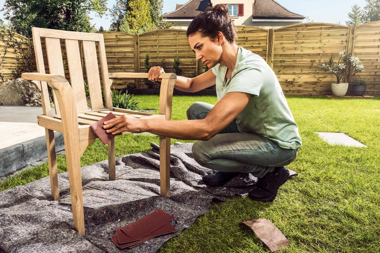 Vrouw schuurt houten stoel in de tuin met schuurpapier