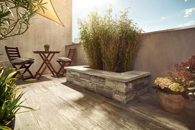 Terras met houten vloer, tafel en stoelen, evenals een plantenbak met beplanting