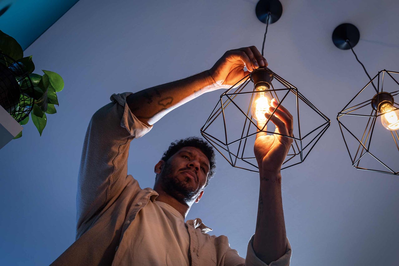Een man draait een brandende LED-lamp in een zwarte, geometrische hanglamp met een modern ontwerp.