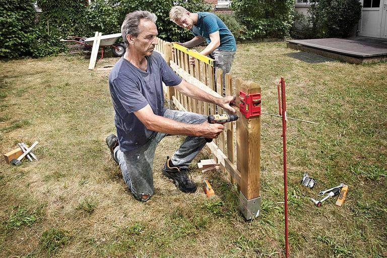 Twee mannen bouwen een houten schutting in de tuin met een accuschroevendraaier en waterpas.