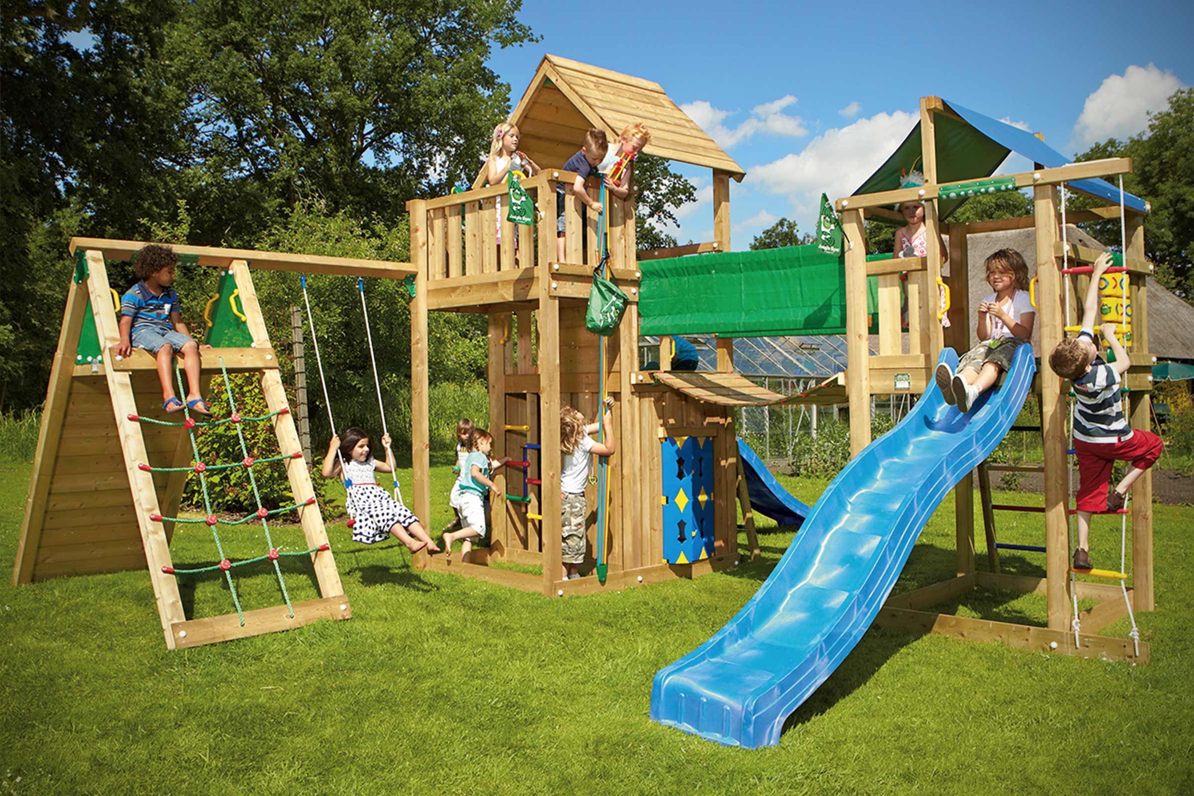 Grote houten speeltoren met glijbaan, schommel en klimwand in de tuin met spelende kinderen.