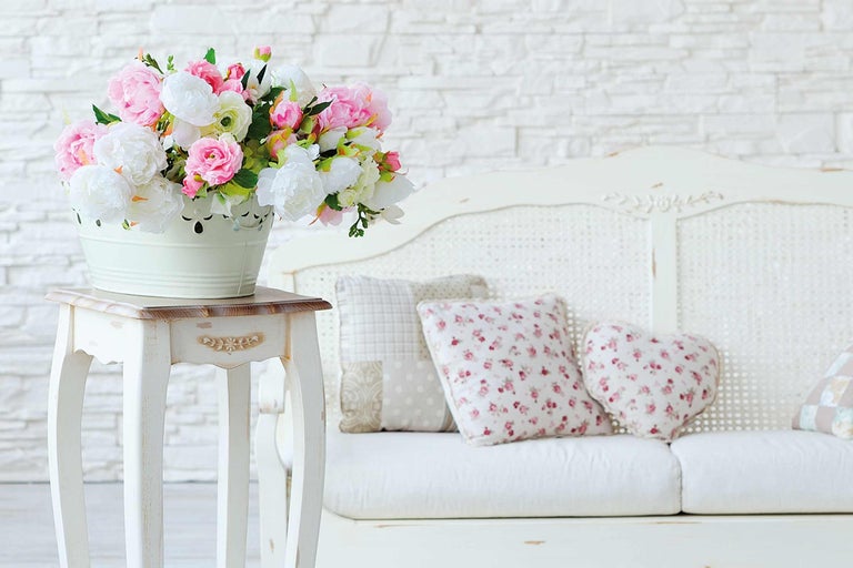 Decoratieve scène met boeket bloemen in een emmer op een bijzettafel naast een bank met kussens