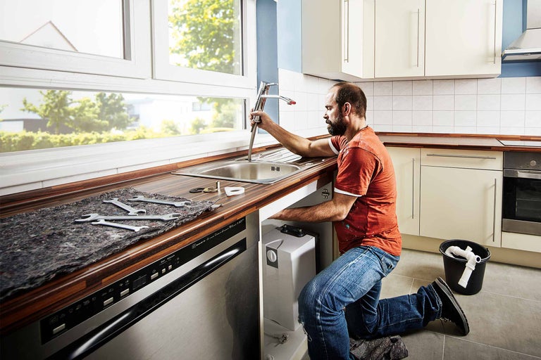 Installateur installeert een keukenkraan in een keuken met spoelbak, werkbladen en keukenapparatuur.