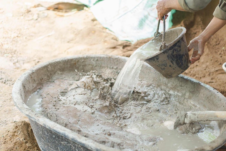Beton mengen in een speciekuip met een emmer water.