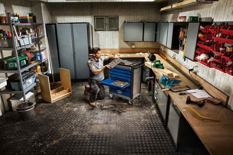 Werkplaats met gereedschapswagen, werkbank en rekken voor gereedschapsopslag.