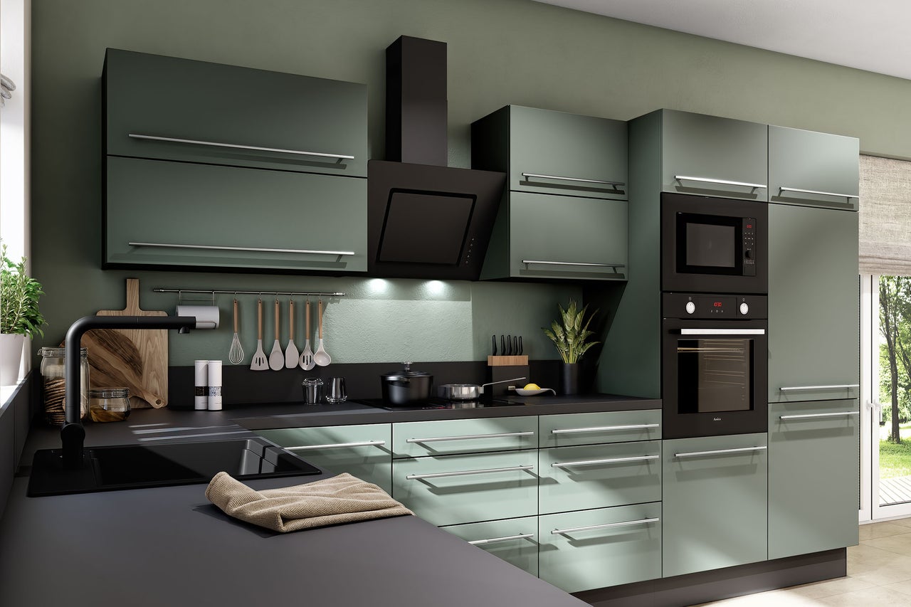 Moderne inbouwkeuken in matgroen met zwart werkblad, oven, magnetron, afzuigkap en zilverkleurige handgrepen.