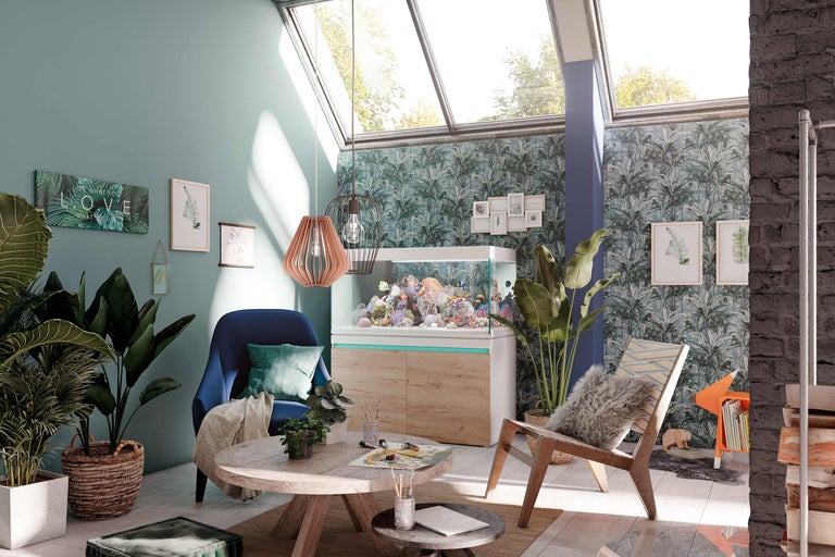 Woonkamer met aquarium, fauteuil, tafel en kamerplanten onder een groot dakraam