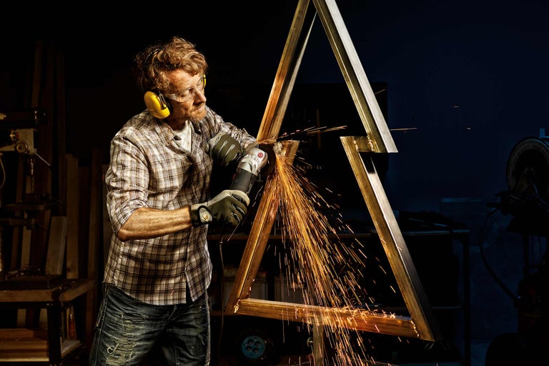 Man slijpt metalen constructie met haakse slijper, vonken vliegen eraf, persoonlijke beschermingsmiddelen worden gedragen.