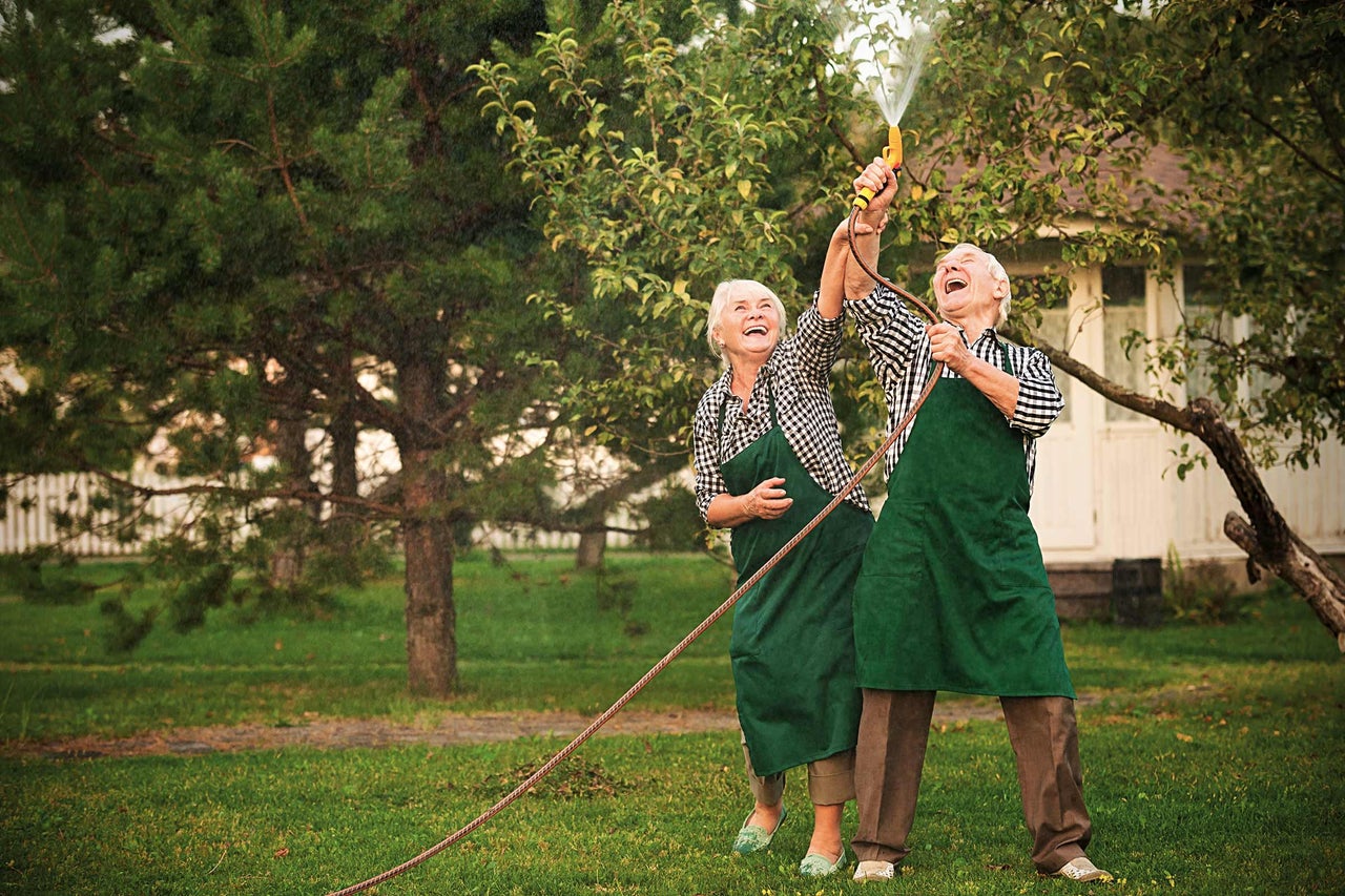 Ouder echtpaar met tuinslang in de tuin
