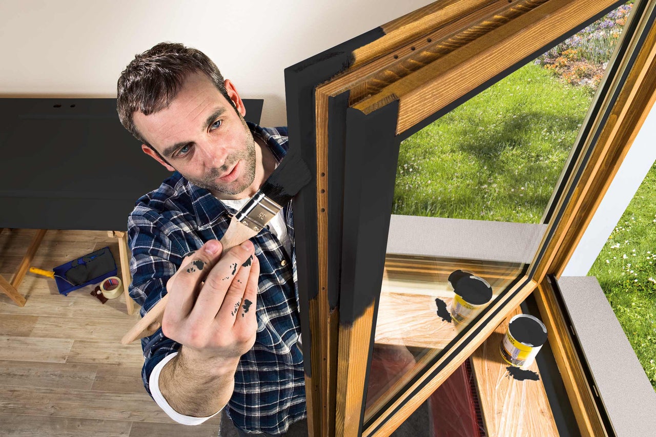 Man schildert houten raamkozijn met een kwast en verf.