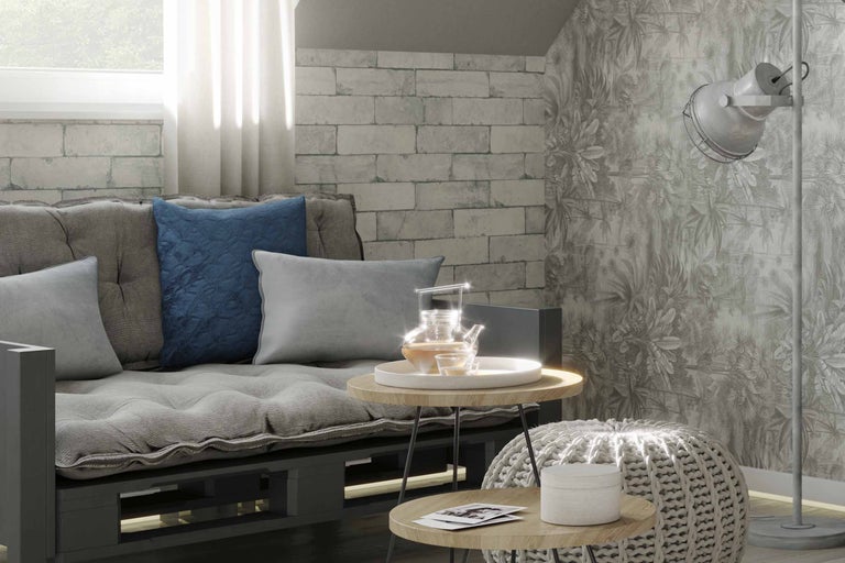 Woonkamer met palletbank, kussens, bijzettafels, gebreide poef en vloerlamp voor een behang met motief