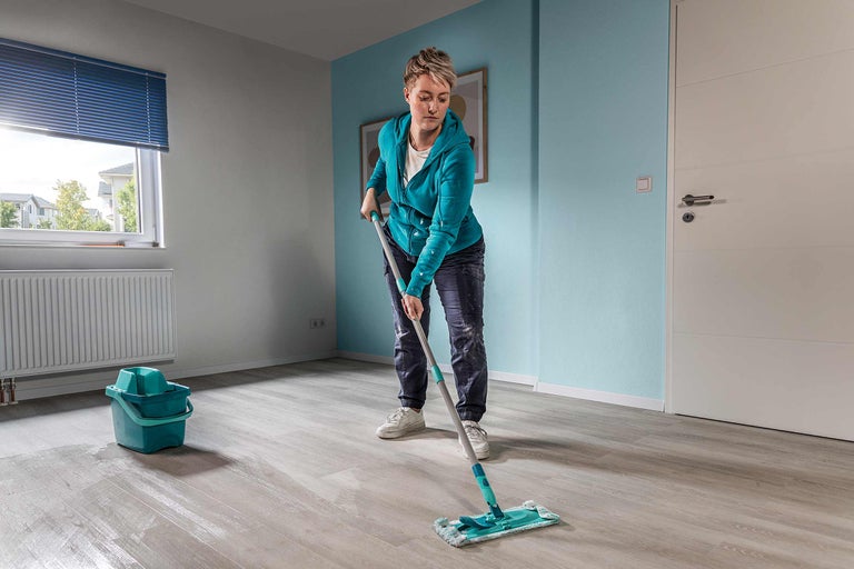 Vrouw dweilt vloer met dweil in een kamer met emmer en radiator