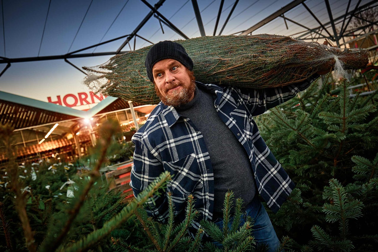 Een man draagt een verpakte kerstboom op zijn schouder in een Hornbach-winkel.