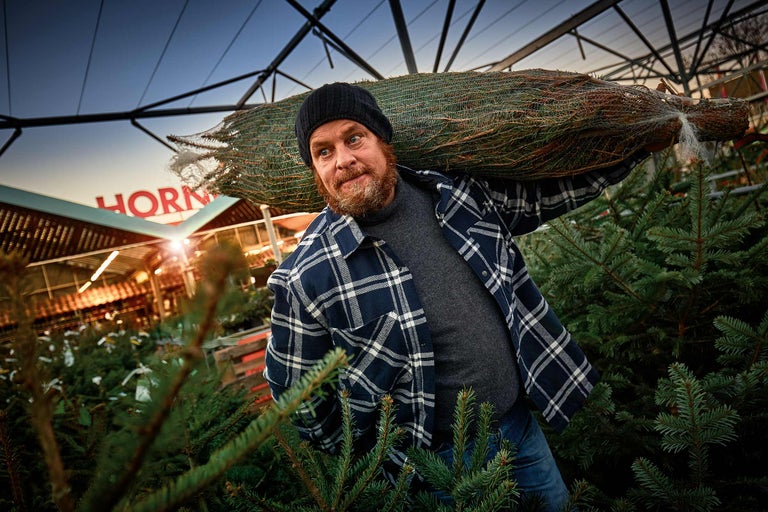 Een man draagt een verpakte kerstboom op zijn schouder in een Hornbach-winkel.
