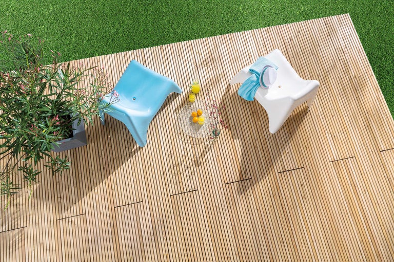 Bovenaanzicht van een houten terras met twee stoelen, een bijzettafel en een pot met bloeiende planten.