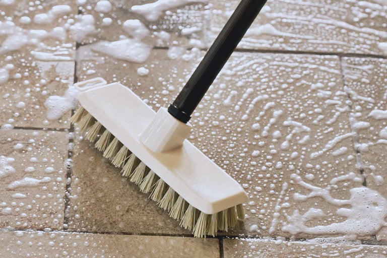 Borstel met steel reinigt tegels met zeepsop