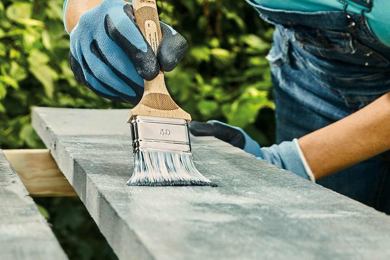 Iemand schildert een houten plank met een kwast.