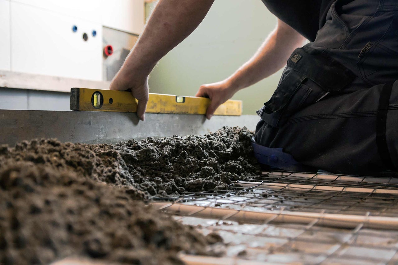Een vakman nivelleert dekvloer met een waterpas op een bouwplaats.