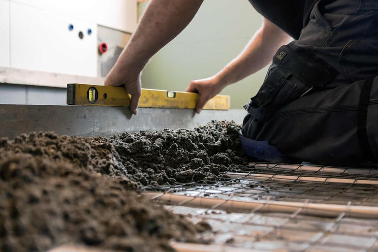 Een vakman nivelleert dekvloer met een waterpas op een bouwplaats.