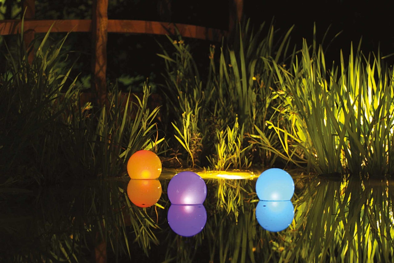 Drie kleurrijke drijvende bollen op een vijver tussen planten verlicht.