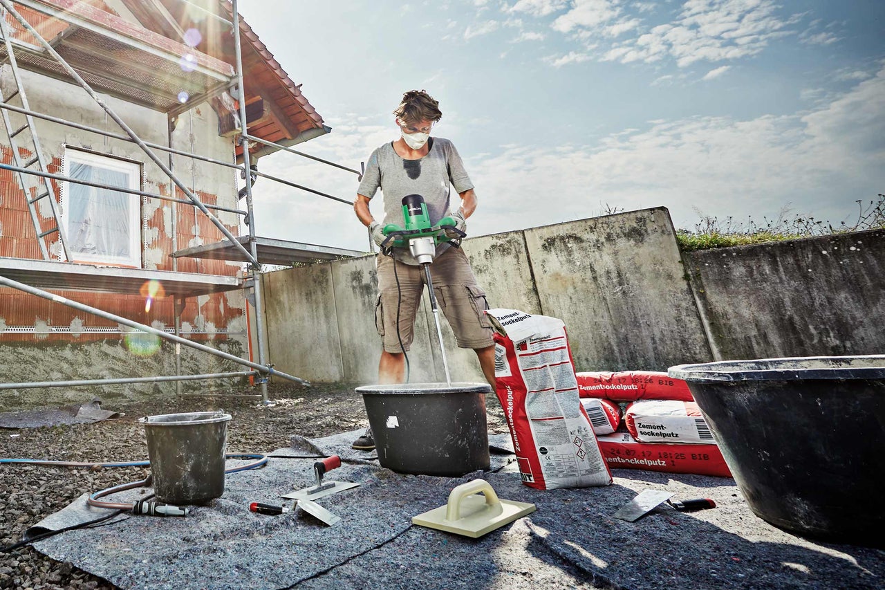 Vakman mengt cement met een elektrische mixer op een bouwplaats.
