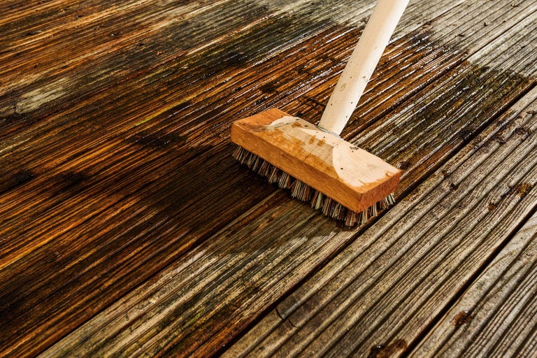 Een borstel reinigt een houten terras.