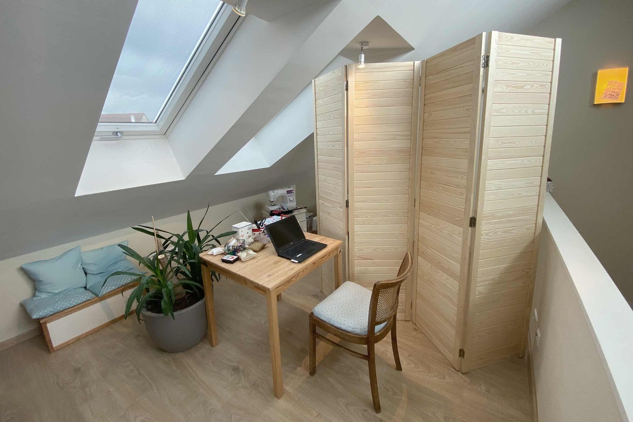 Inrichting van een zolderkantoor met houten bureau, laptop, kamerplant, houten stoel en kamerscherm.