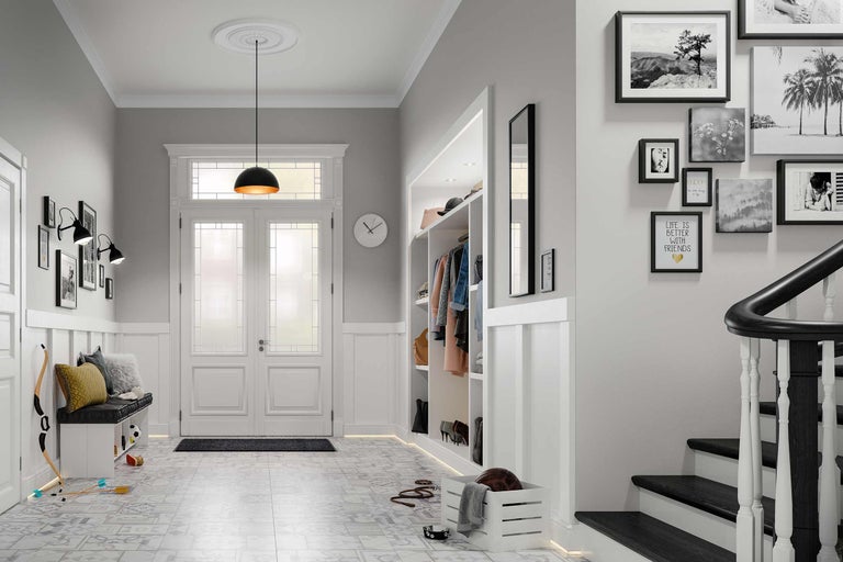 Lichte hal met garderobe, zitbank, trap en decoratieve elementen zoals schilderijen en een hanglamp.
