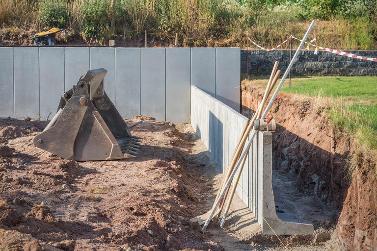 Bouwplaats met betonnen muur, graafbak en gereedschap in een bouwput.