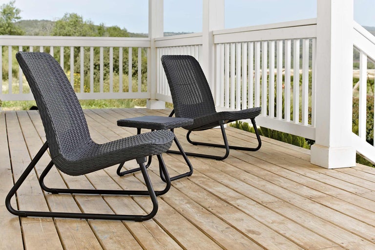 Twee rotan stoelen en een tafel op een houten terras.