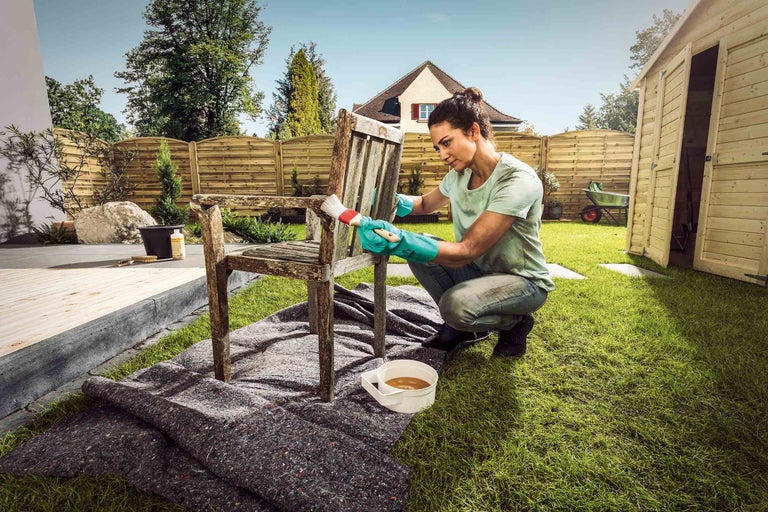 Vrouw schildert een houten stoel met een borstel in de tuin.