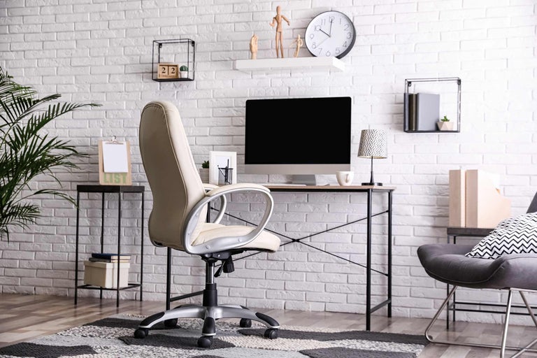 Lichte werkkamer met bureau, bureaustoel en decoratieve elementen voor een witte bakstenen muur